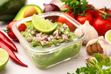 Photo of Bowl of delicious guacamole with onion, lime and ingredients on white wooden table, closeup