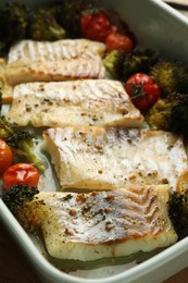 Pieces of delicious baked cod with vegetables and spices in dish, closeup