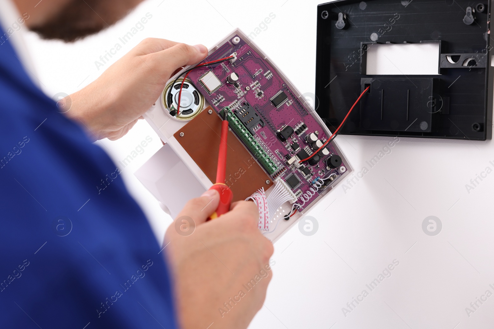 Photo of Man installing home security alarm system on white wall indoors, closeup