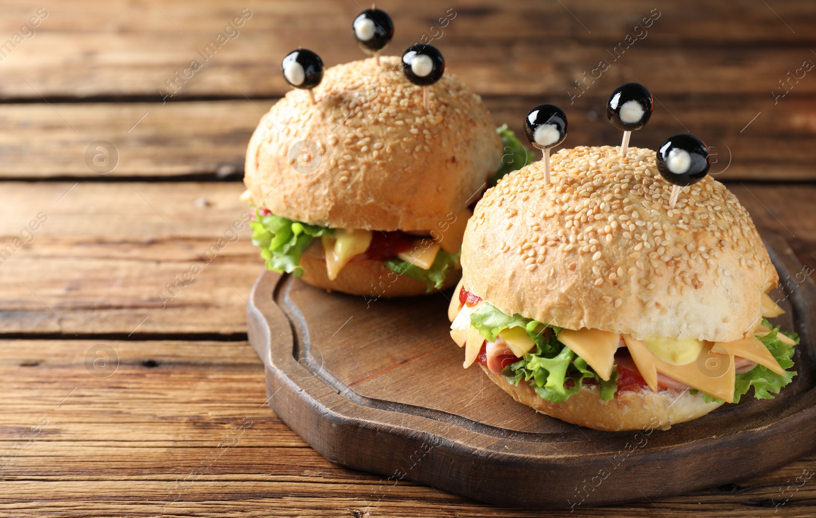 Photo of Cute monster burgers served on wooden table. Halloween party food