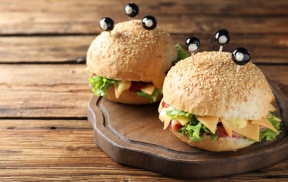 Photo of Cute monster burgers served on wooden table. Halloween party food