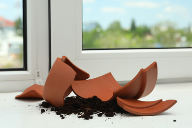 Broken terracotta flower pot with soil on white windowsill indoors