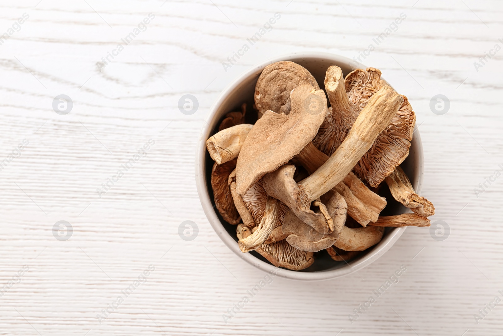 Photo of Bowl of dried mushrooms on wooden background, top view with space for text