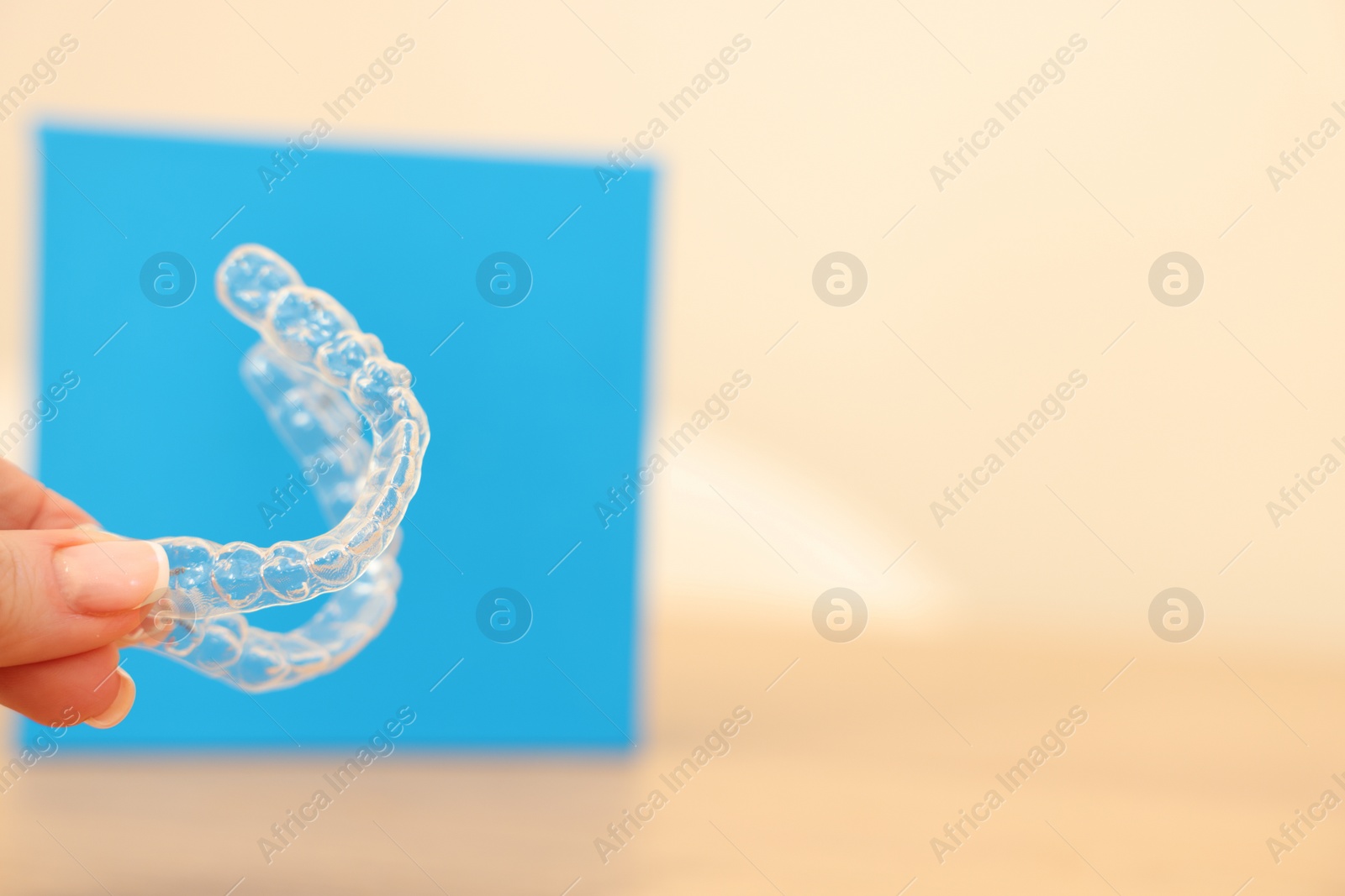 Photo of Woman with transparent dental aligners on blurred background, closeup. Space for text