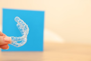 Photo of Woman with transparent dental aligners on blurred background, closeup. Space for text