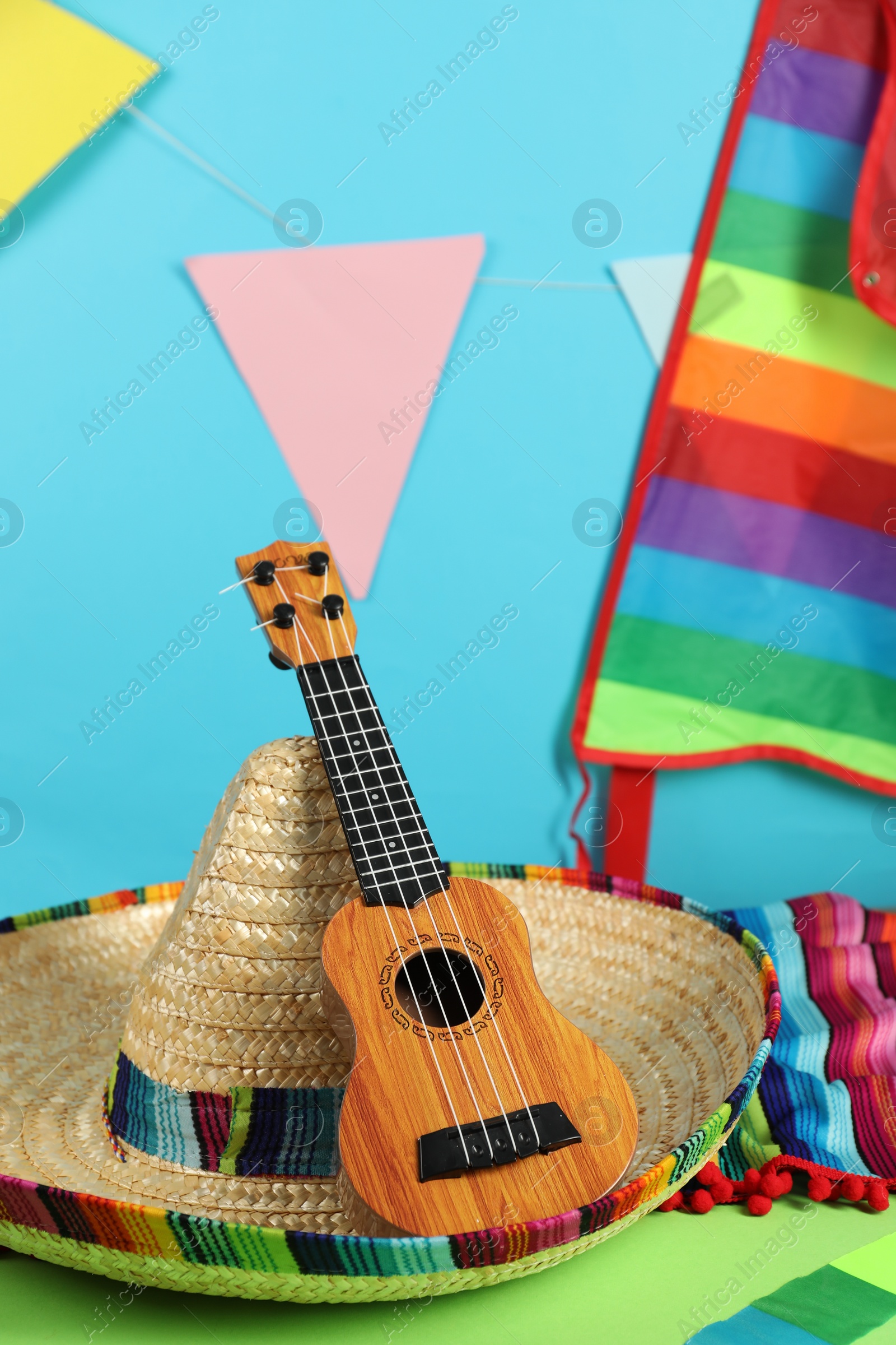 Photo of Mexican sombrero hat and ukulele on green table, closeup