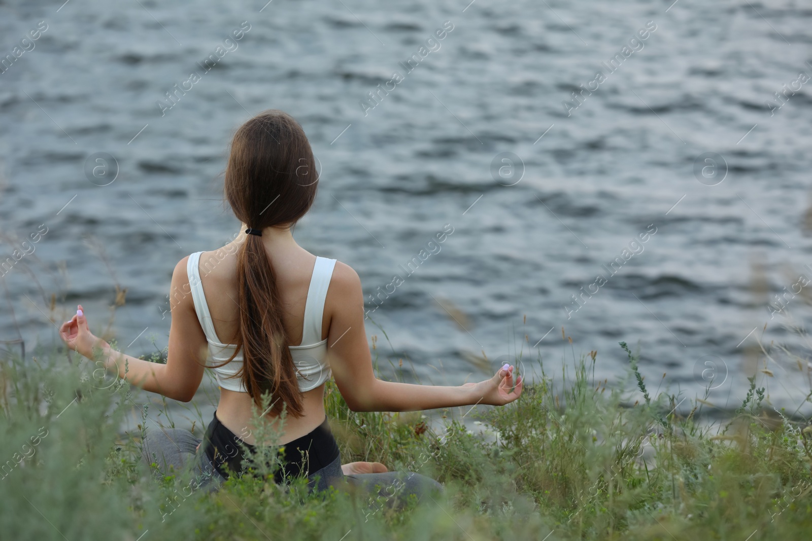 Photo of Teenage girl meditating near river, back view. Space for text