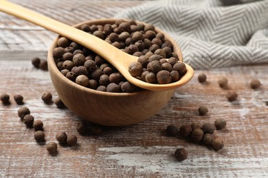 Photo of Aromatic allspice pepper grains in bowl and spoon on wooden table, closeup