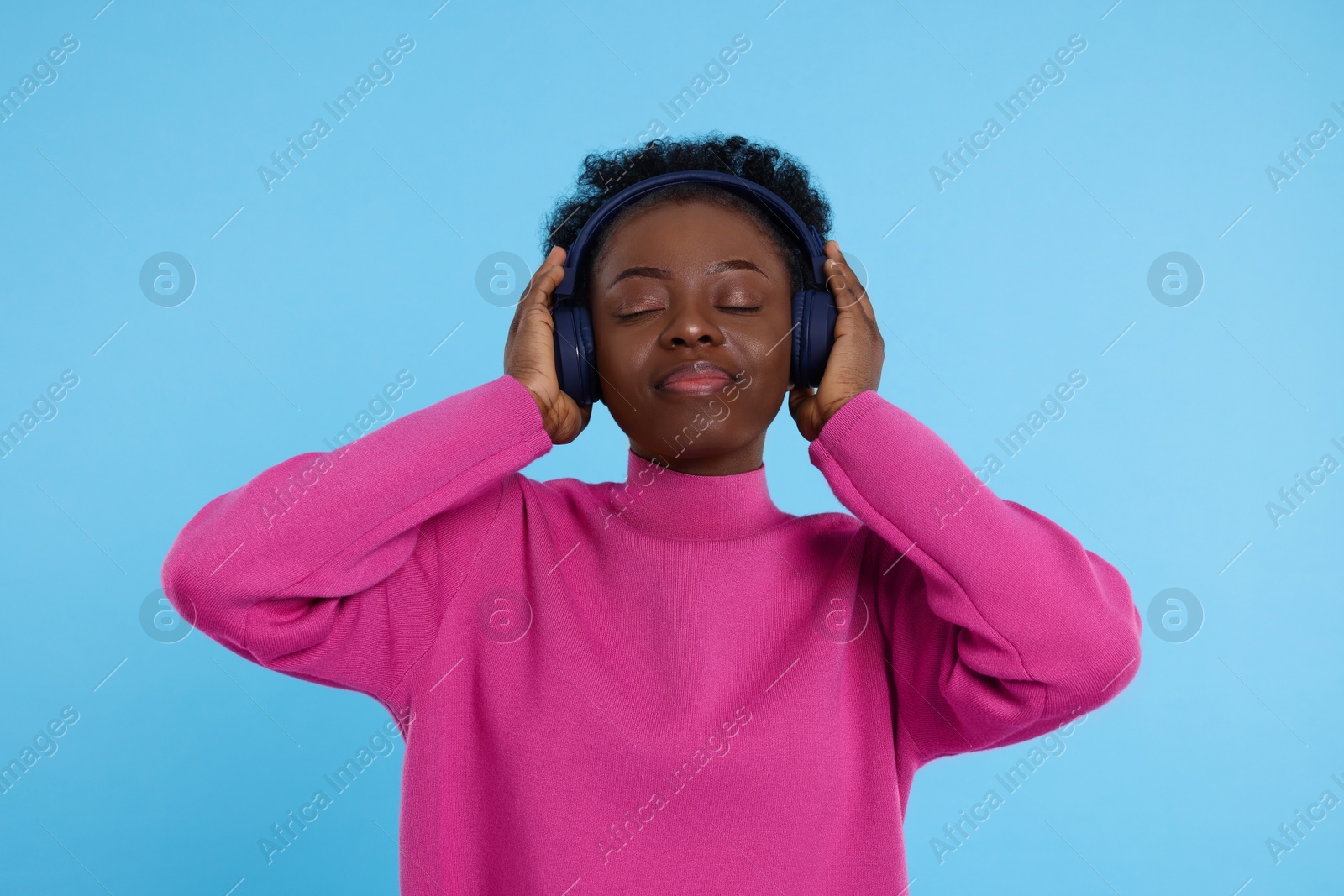 Photo of Young woman in headphones enjoying music on light blue background