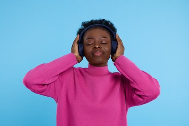 Young woman in headphones enjoying music on light blue background