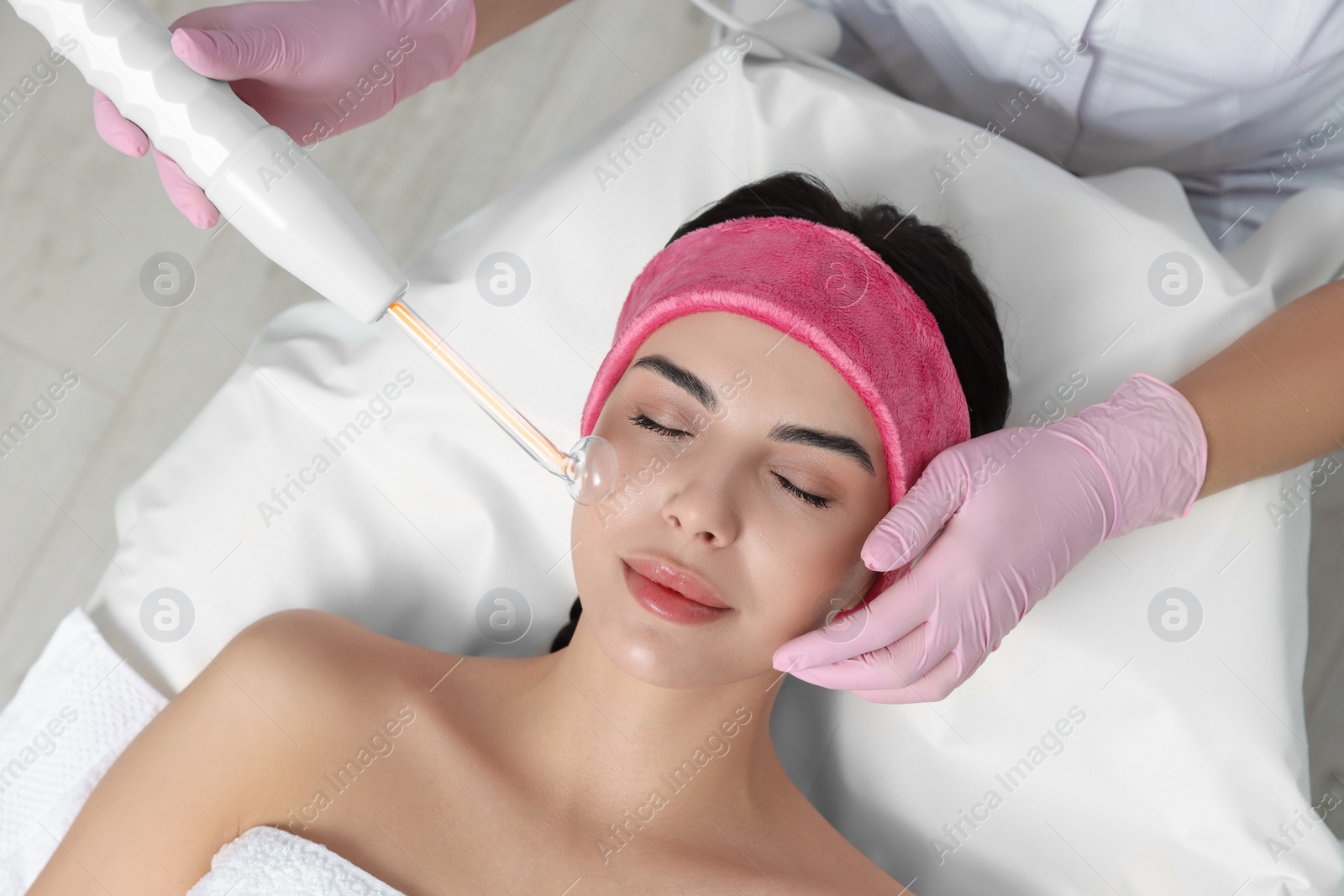 Photo of Young woman undergoing face rejuvenation procedure with darsonval in salon, top view