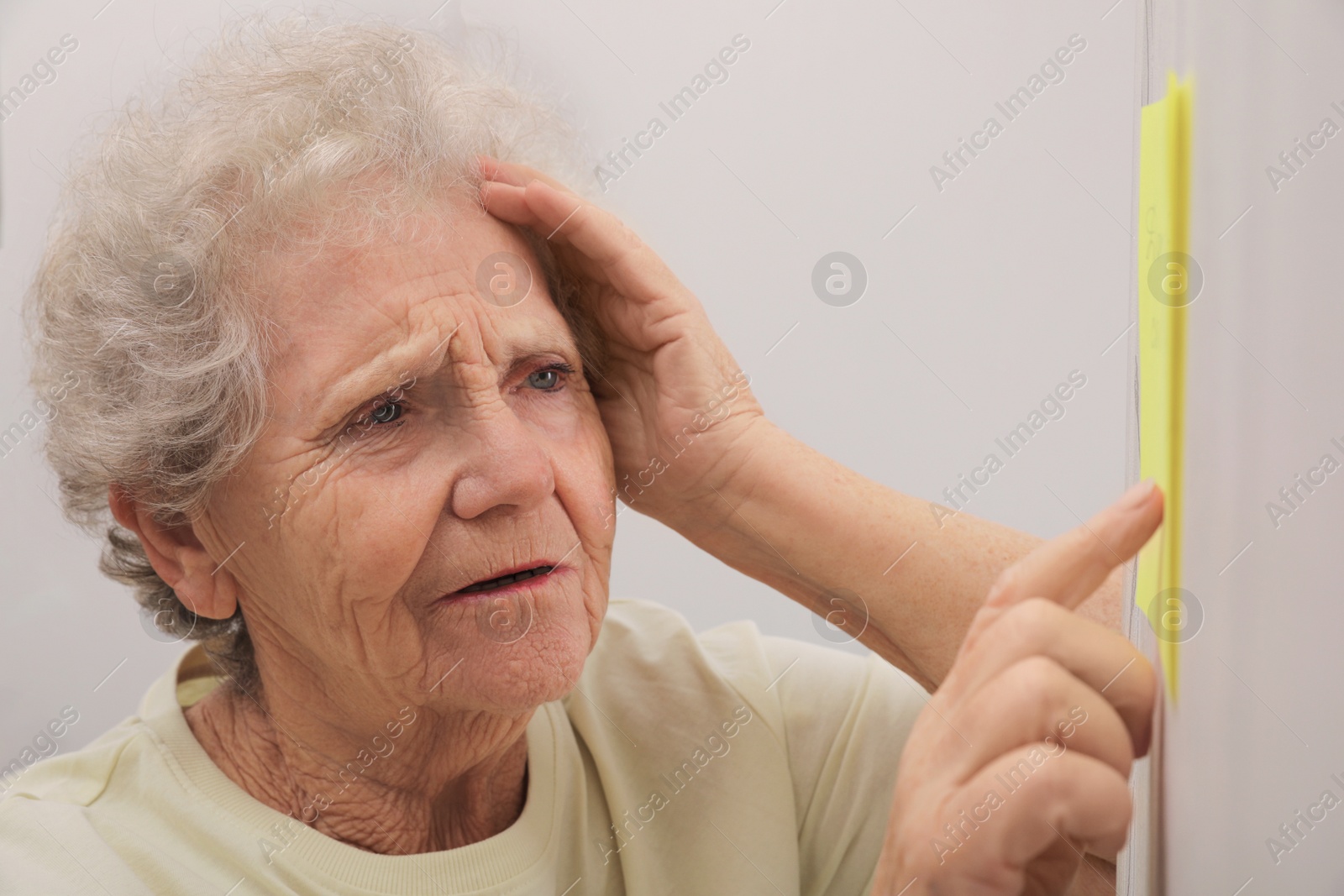 Photo of Senior woman looking at reminder note indoors. Age-related memory impairment