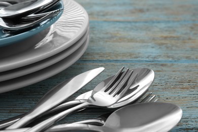 Photo of Silver clean spoons, forks and knives with plates on old light blue wooden table, closeup