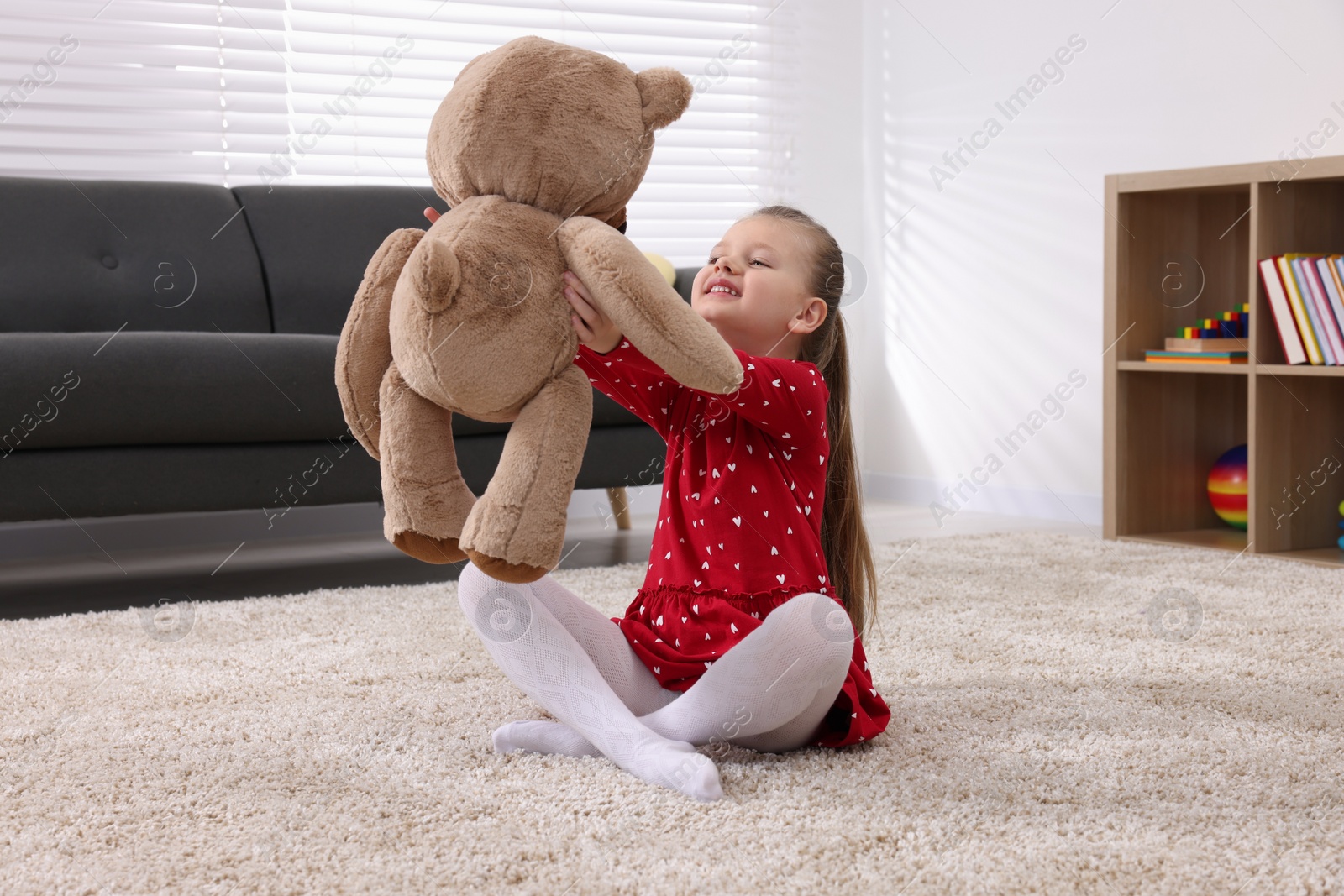 Photo of Cute little girl playing with teddy bear at home