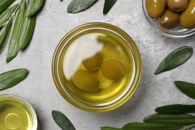 Cooking oil, olives and leaves on light gray textured table, flat lay