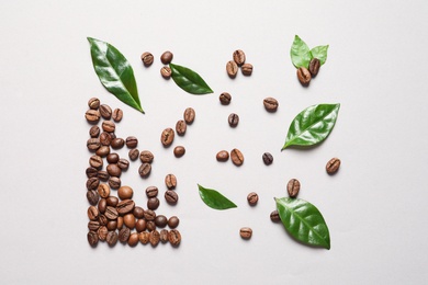 Fresh green coffee leaves and beans on light background, flat lay