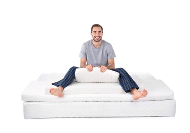 Young man sitting on mattress pile against white background