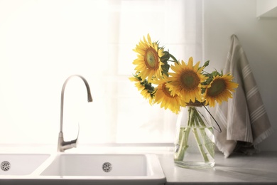 Photo of Vase with beautiful yellow sunflowers in kitchen