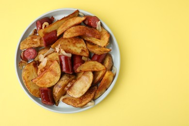 Photo of Delicious baked potato with thin dry smoked sausages and onion on yellow table, top view. Space for text