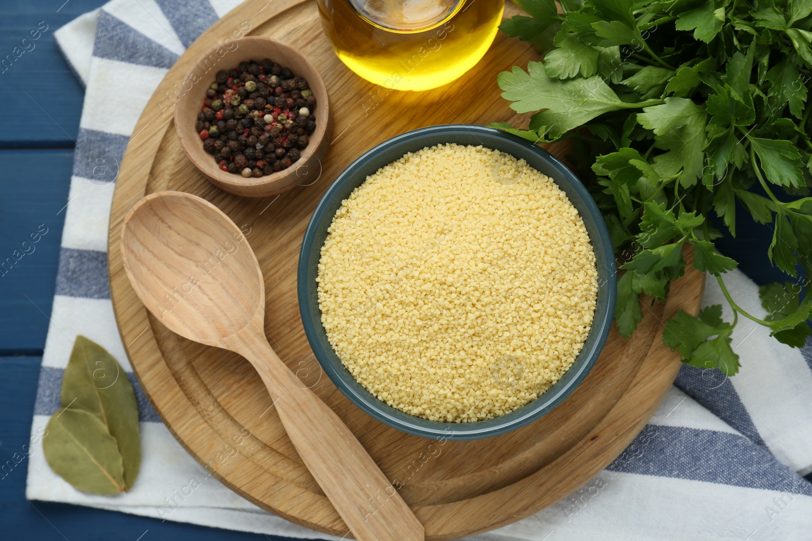 Photo of Bowl of raw couscous and ingredients on blue wooden table, flat lay