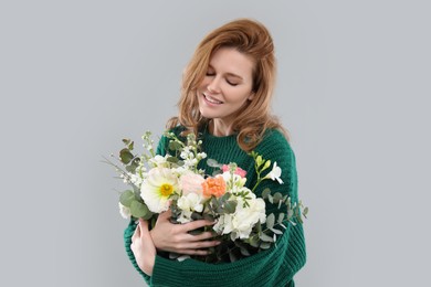 Beautiful woman with bouquet of flowers on grey background