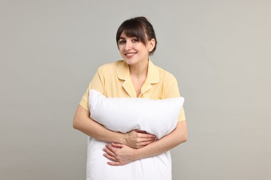 Photo of Happy woman in pyjama holding pillow on grey background