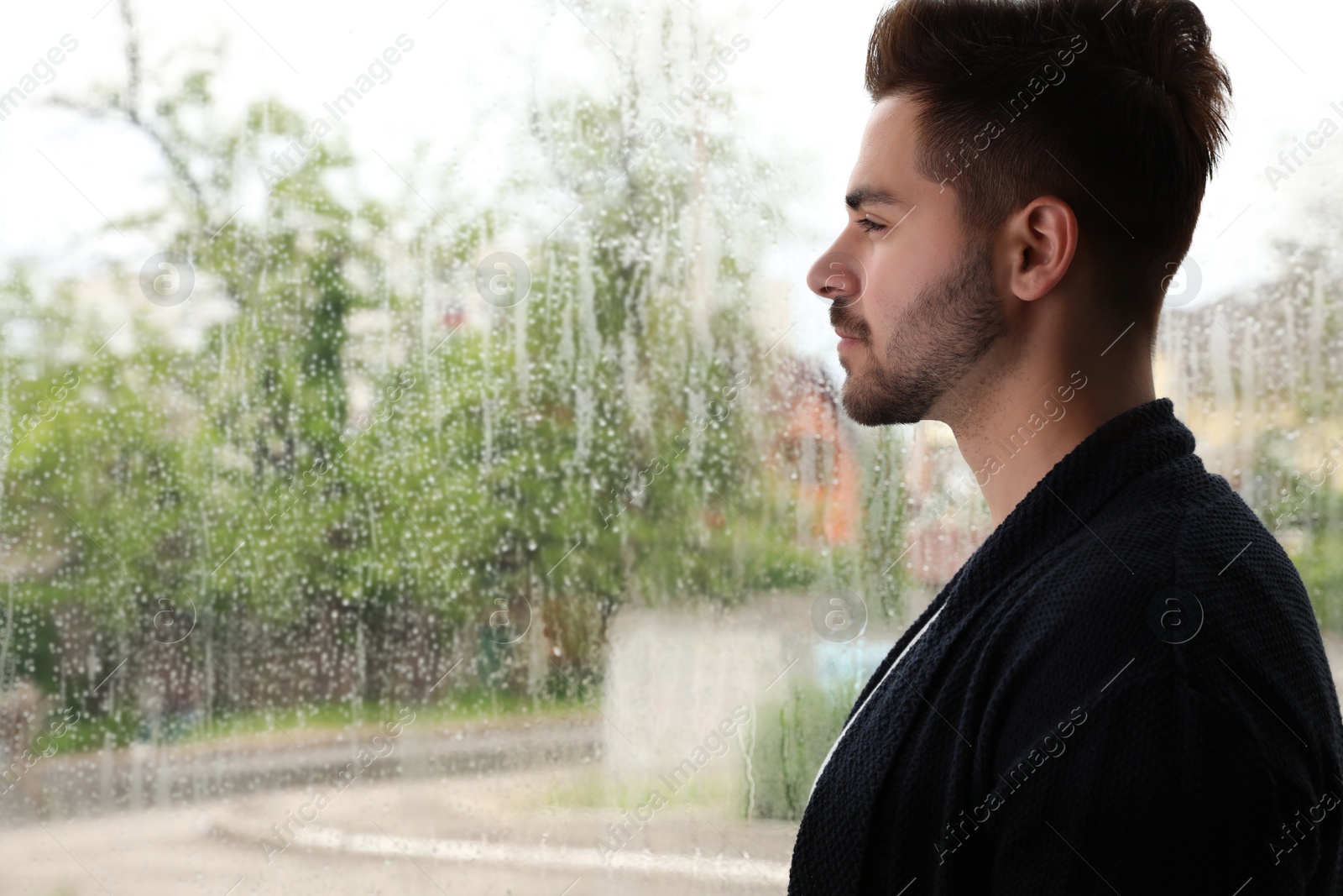 Photo of Thoughtful handsome man near window indoors on rainy day