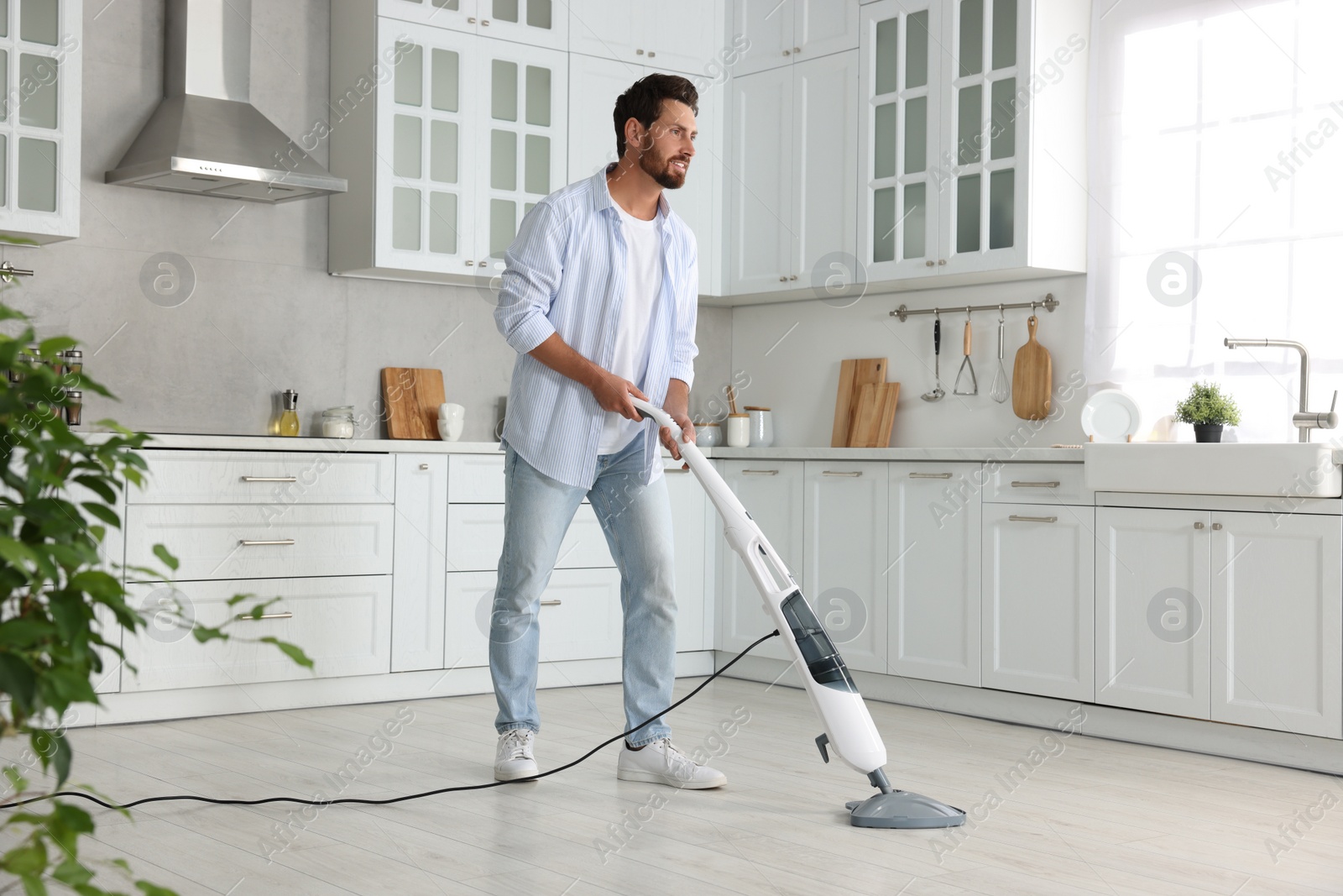 Photo of Happy man cleaning floor with steam mop in kitchen at home