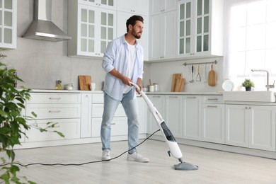 Happy man cleaning floor with steam mop in kitchen at home