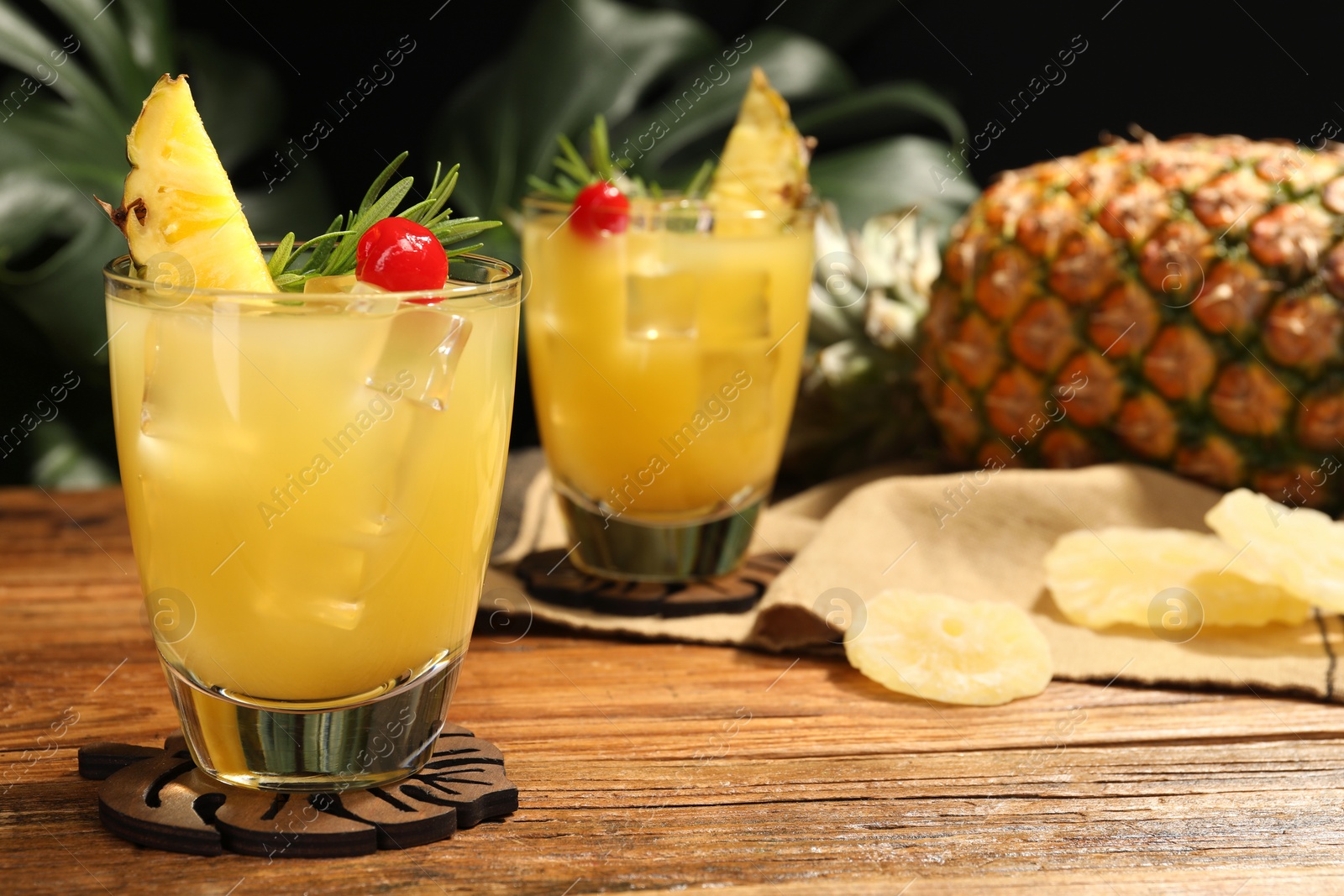 Photo of Glasses of tasty pineapple cocktail with rosemary and cherry on wooden table. Space for text