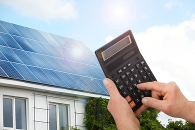 Image of Man using calculator against house with installed solar panels. Renewable energy and money saving