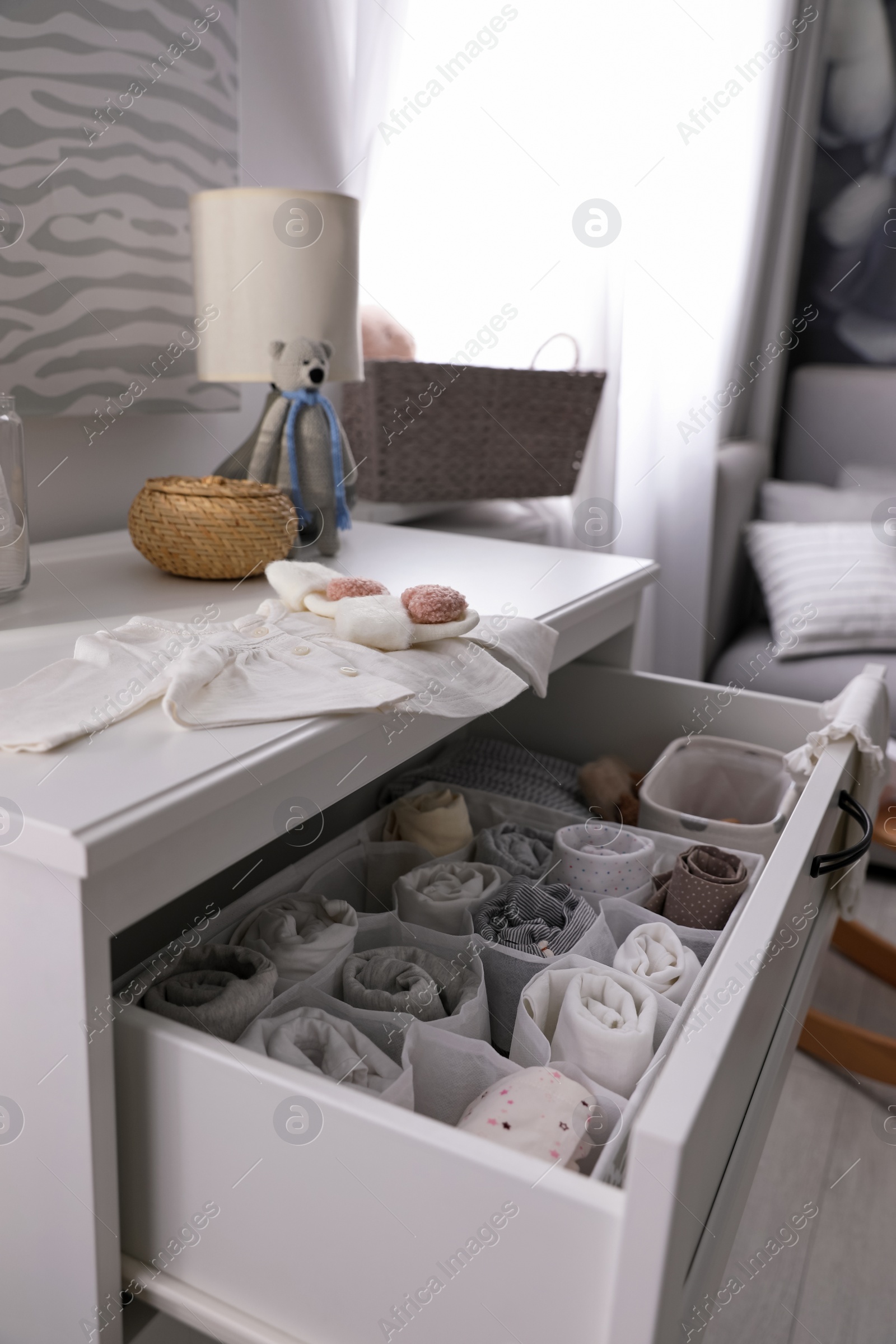 Photo of Modern open chest of drawers with baby clothes and accessories in room