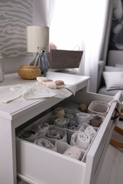 Modern open chest of drawers with baby clothes and accessories in room