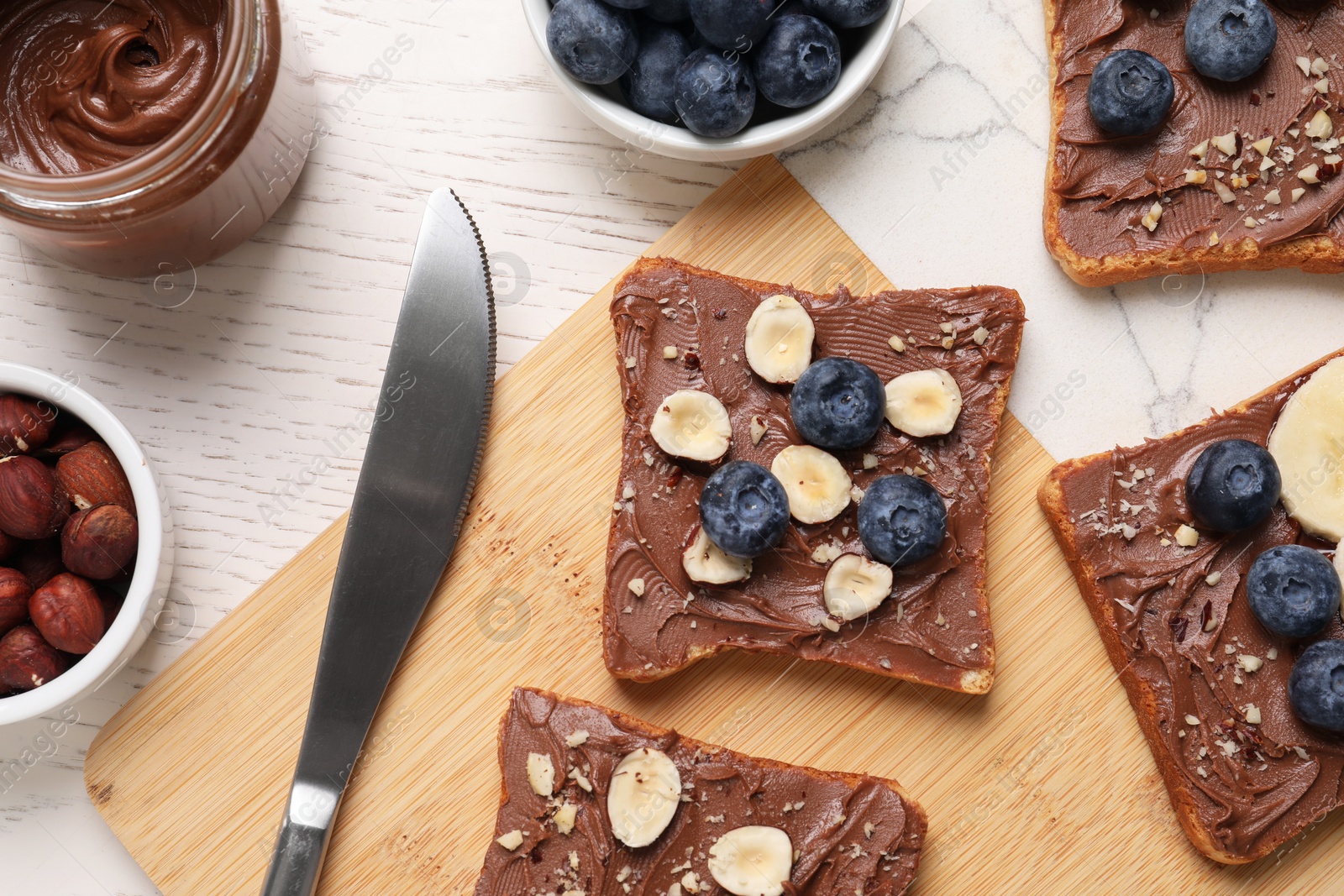 Photo of Different tasty toasts with nut butter and products on white wooden table, flat lay