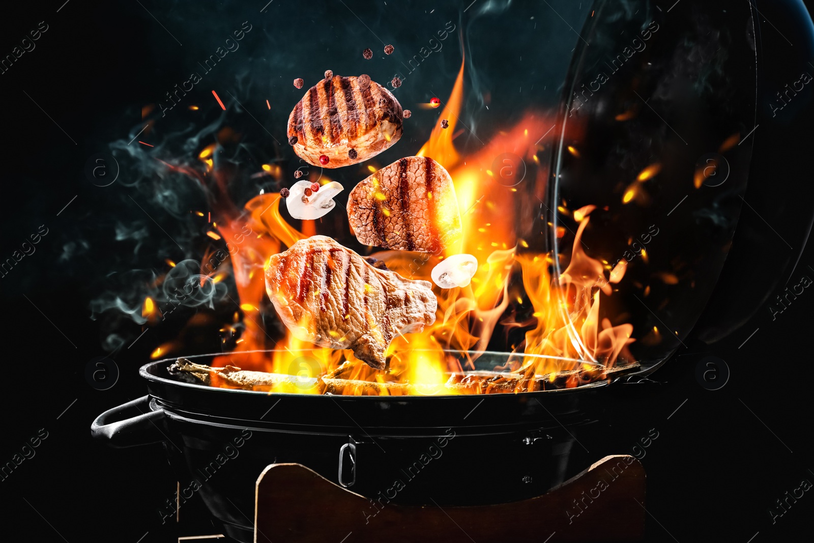 Image of Meat and mushrooms falling onto barbecue grill with flame against black background, closeup