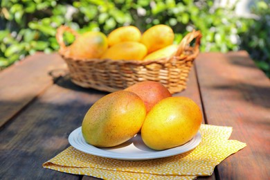 Plate with tasty mangoes on wooden table outdoors