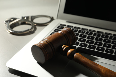 Photo of Laptop, wooden gavel and handcuffs on grey table, closeup. Cyber crime