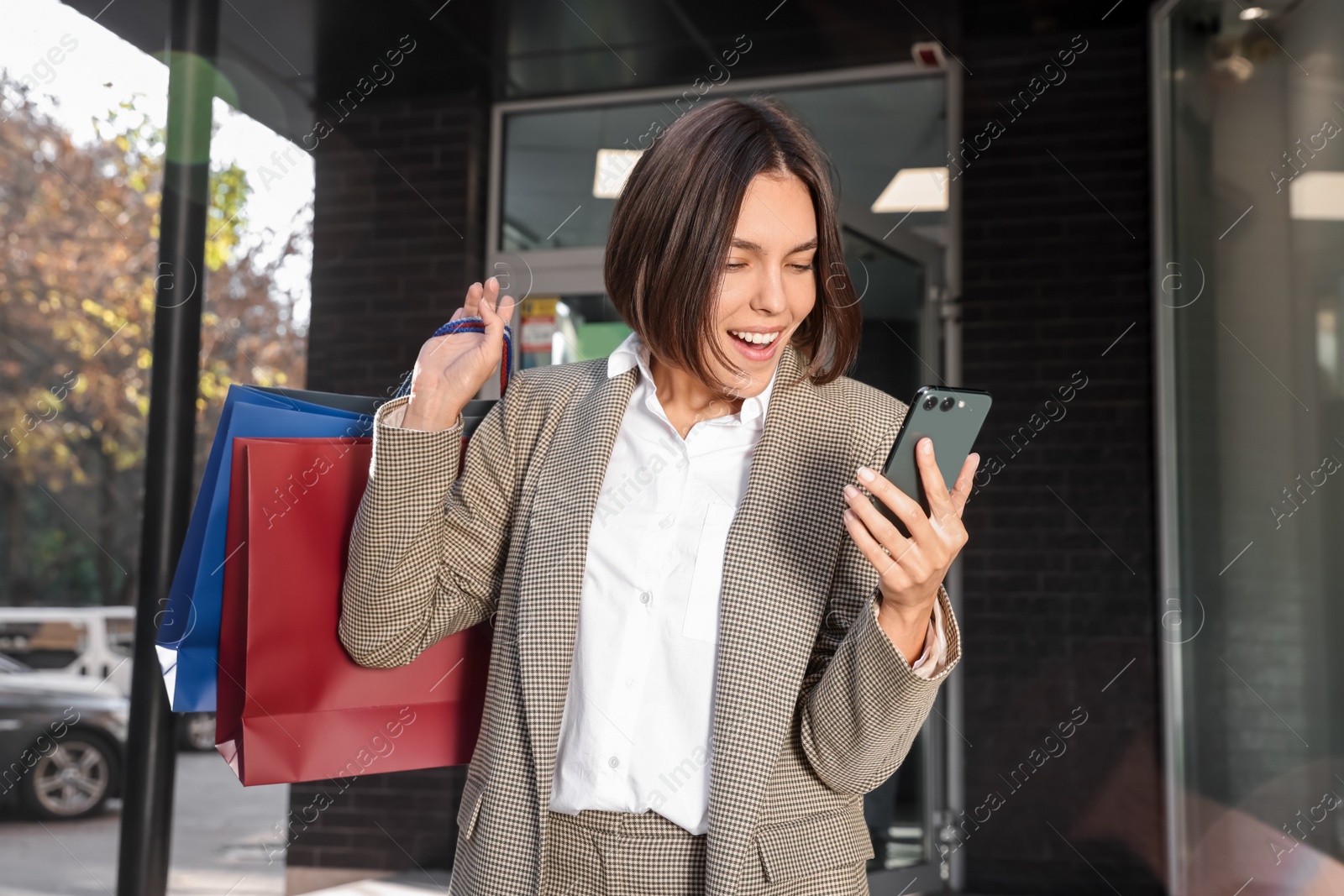 Photo of Special Promotion. Emotional young woman with shopping bags and smartphone on city street