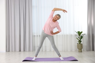 Photo of Happy senior woman practicing yoga on mat at home