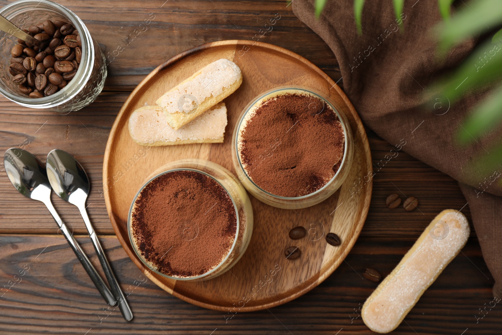 Photo of Delicious tiramisu in glasses served on wooden table, flat lay