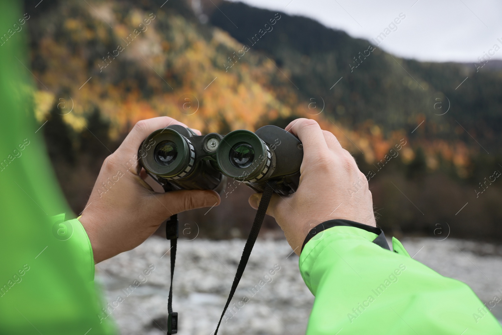 Photo of Woman holding binoculars near river in beautiful mountains, closeup