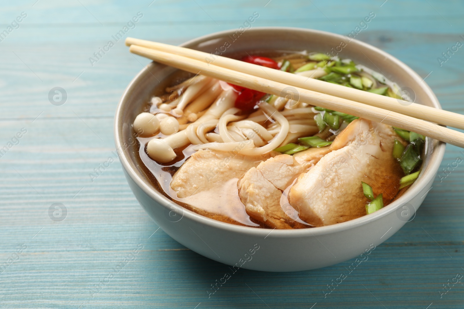 Photo of Delicious ramen with meat in bowl and chopsticks on light blue wooden table, closeup. Space for text