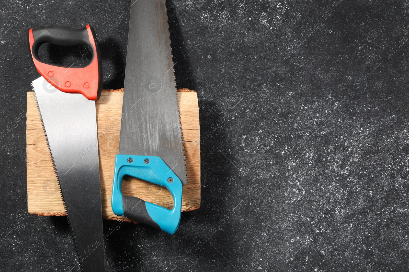Photo of Saws with colorful handles and log on dark gray textured background, flat lay. Space for text