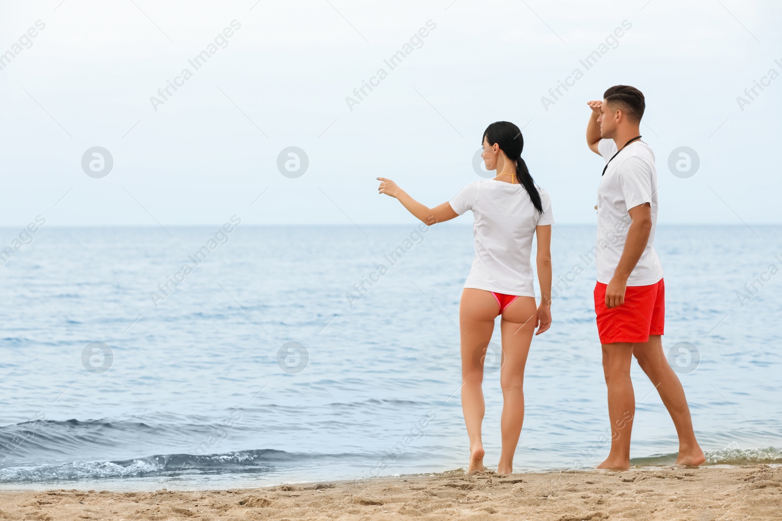 Photo of Professional lifeguards working at sandy beach, back view