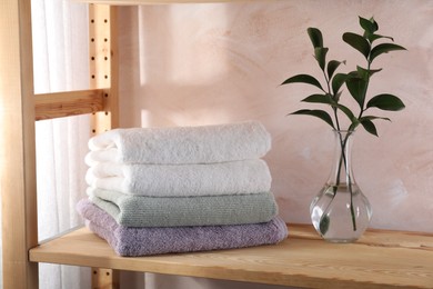 Photo of Stacked soft towels and green leaves on wooden shelf indoors