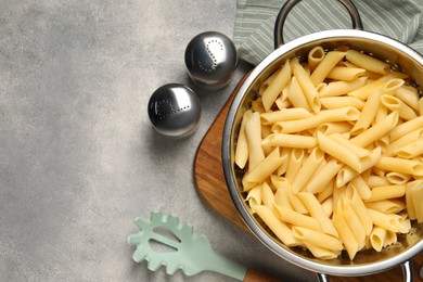 Delicious penne pasta in colander, spices and spoon on gray table, flat lay. Space for text