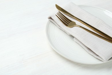 Photo of Stylish ceramic plate, cutlery and napkin on white wooden table, closeup. Space for text