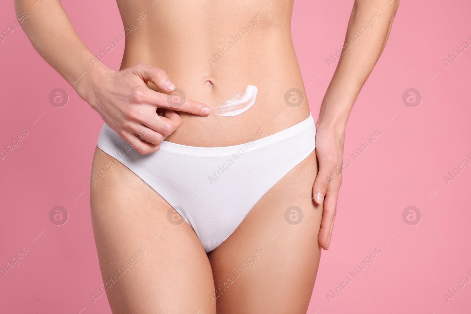 Photo of Woman applying body cream onto her belly against pink background, closeup