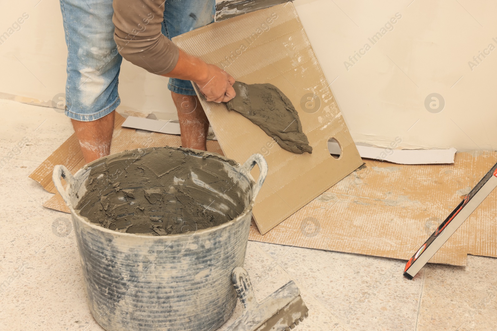 Photo of Worker spreading adhesive mix over tile with spatula, closeup