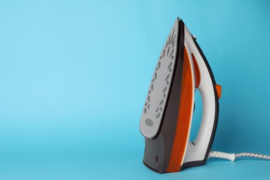 Photo of One modern iron on light blue background, space for text. Home appliance